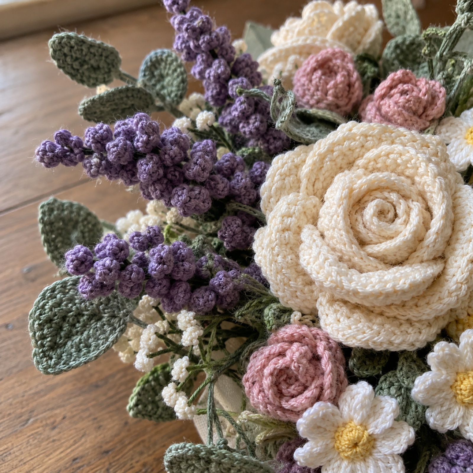 Close-up of the lavender sprigs made of tiny bobble stitches beside a cream rose on the Wildflower Bridal Bouquet